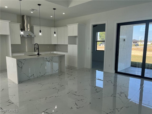 kitchen featuring white cabinetry, sink, wall chimney exhaust hood, light stone counters, and an island with sink