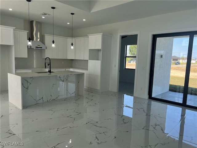 kitchen featuring wall chimney exhaust hood, a sink, a kitchen island with sink, and white cabinets