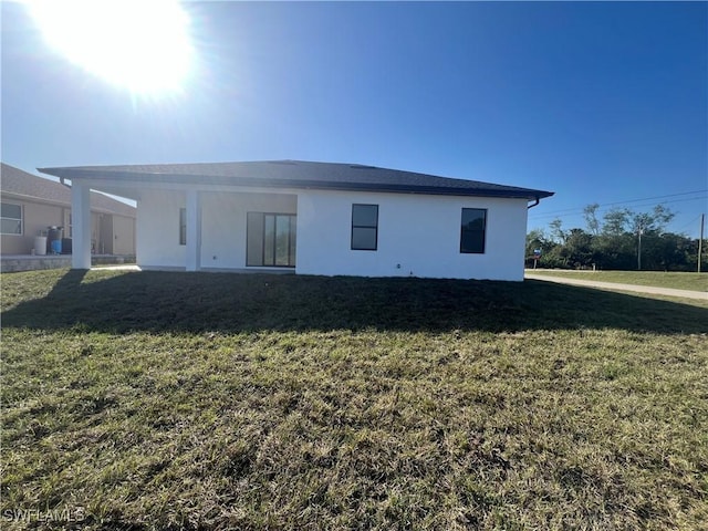 back of property with stucco siding and a yard