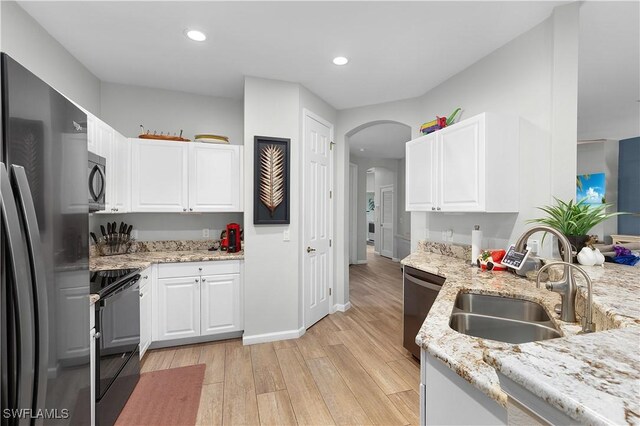 kitchen featuring arched walkways, light stone counters, black appliances, white cabinetry, and a sink