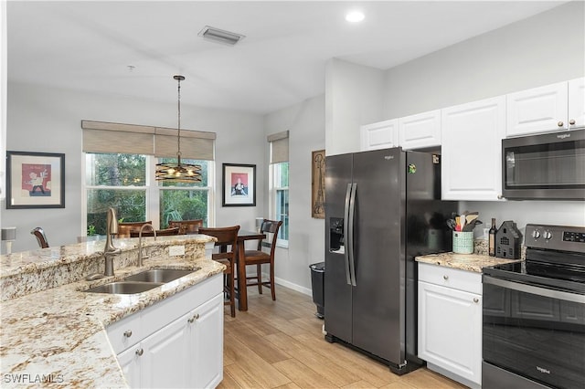 kitchen featuring stainless steel appliances, sink, light hardwood / wood-style flooring, white cabinets, and hanging light fixtures