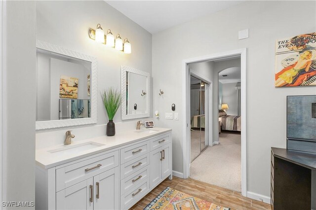 full bathroom with double vanity, wood finished floors, a sink, and baseboards