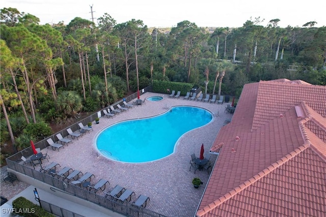 community pool featuring a patio, a wooded view, and fence