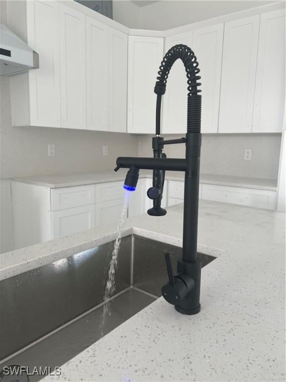 details featuring white cabinets, light stone counters, and wall chimney exhaust hood