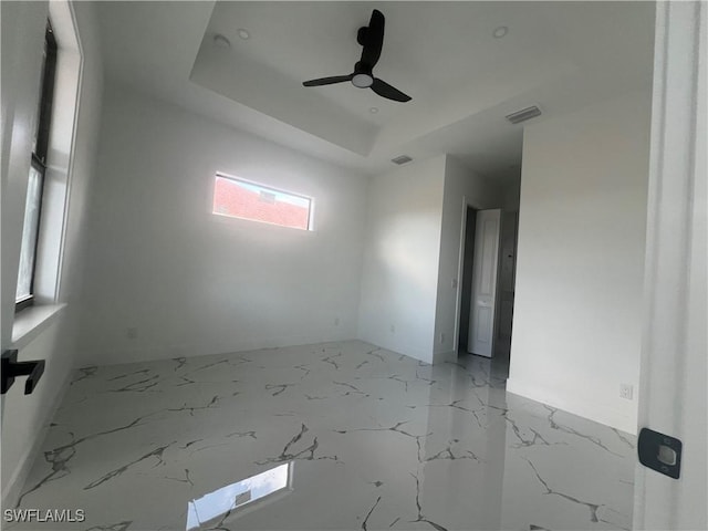 empty room with ceiling fan and a tray ceiling