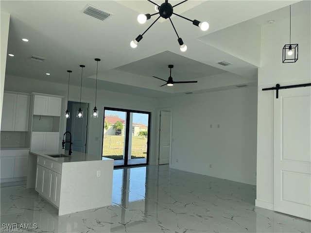 kitchen featuring a barn door, a kitchen island with sink, white cabinetry, and a sink