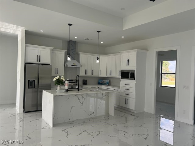 kitchen featuring a center island with sink, hanging light fixtures, stainless steel appliances, wall chimney range hood, and white cabinetry