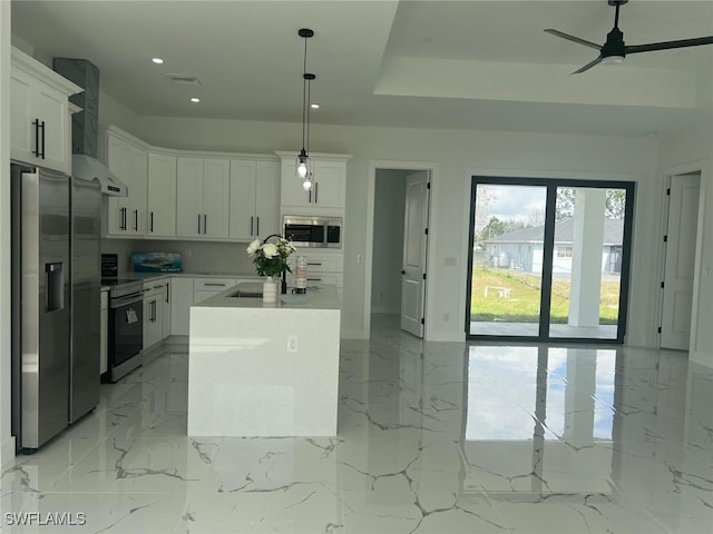 kitchen featuring pendant lighting, stainless steel appliances, white cabinets, an island with sink, and wall chimney exhaust hood