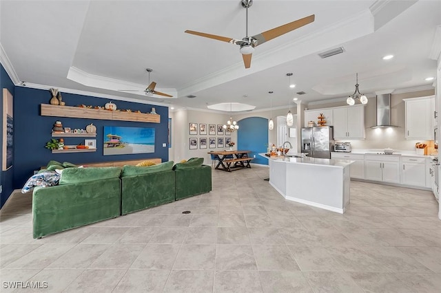 kitchen with stainless steel fridge, a kitchen island with sink, crown molding, wall chimney range hood, and pendant lighting