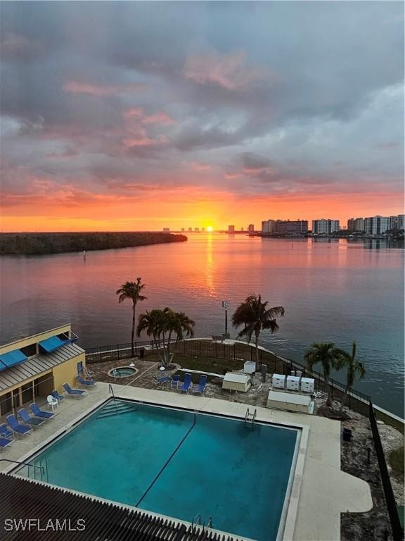 pool at dusk featuring a water view and a patio