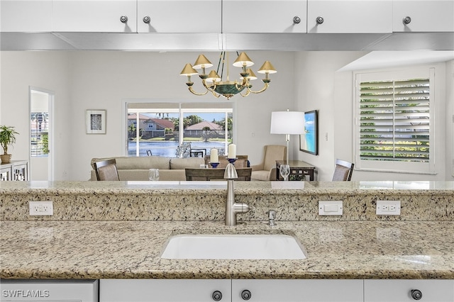 kitchen with pendant lighting, white cabinets, sink, light stone counters, and a chandelier