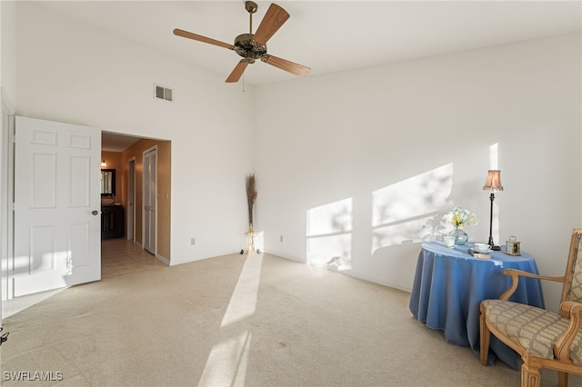 interior space with ceiling fan, light colored carpet, and a high ceiling