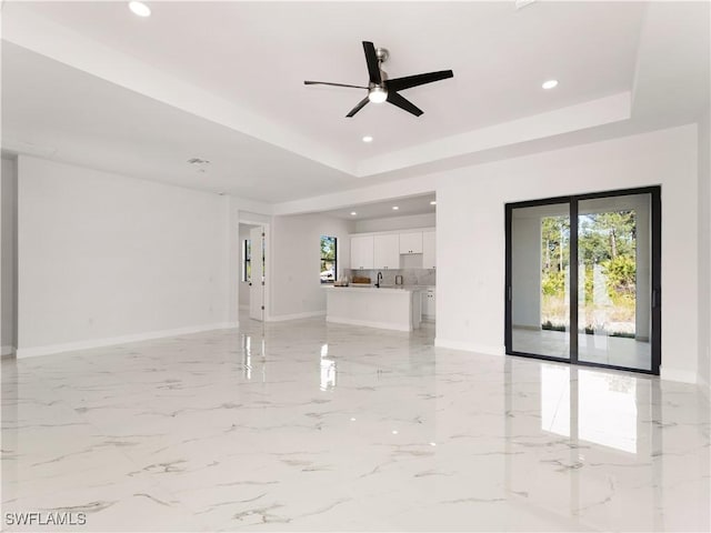 unfurnished living room with a tray ceiling, ceiling fan, and sink