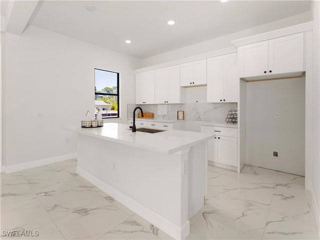 kitchen featuring white cabinets, decorative backsplash, a kitchen island with sink, and sink