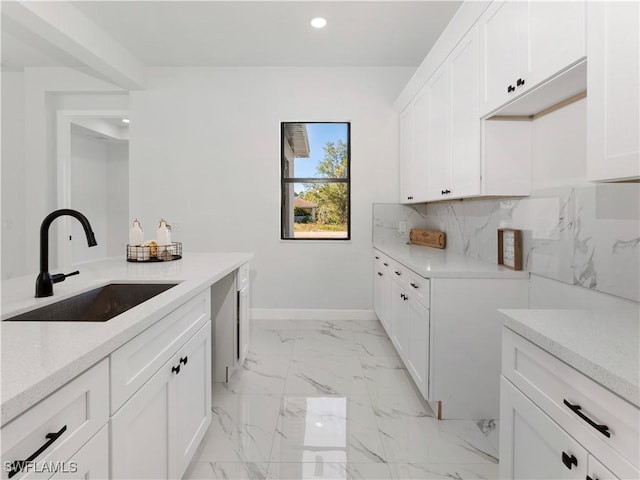 kitchen with backsplash, light stone counters, sink, and white cabinets