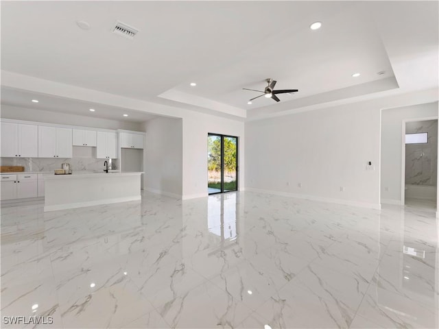 unfurnished living room with a tray ceiling, ceiling fan, and sink