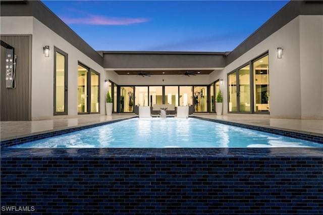 pool at dusk featuring ceiling fan and a patio area