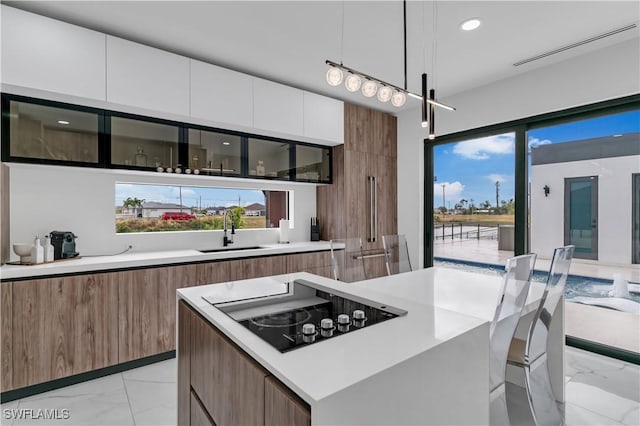 kitchen featuring white cabinets, sink, hanging light fixtures, black electric cooktop, and a kitchen island