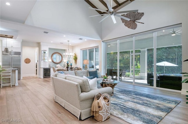 living room featuring wine cooler, high vaulted ceiling, ceiling fan with notable chandelier, and light wood-type flooring