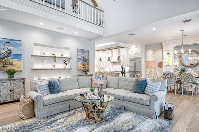 living room with light wood-type flooring, sink, a towering ceiling, and an inviting chandelier