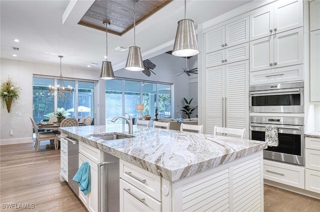 kitchen with sink, a center island with sink, light hardwood / wood-style floors, white cabinetry, and hanging light fixtures