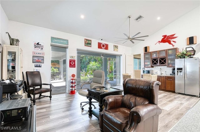 living room featuring ceiling fan, wet bar, light wood-type flooring, and high vaulted ceiling