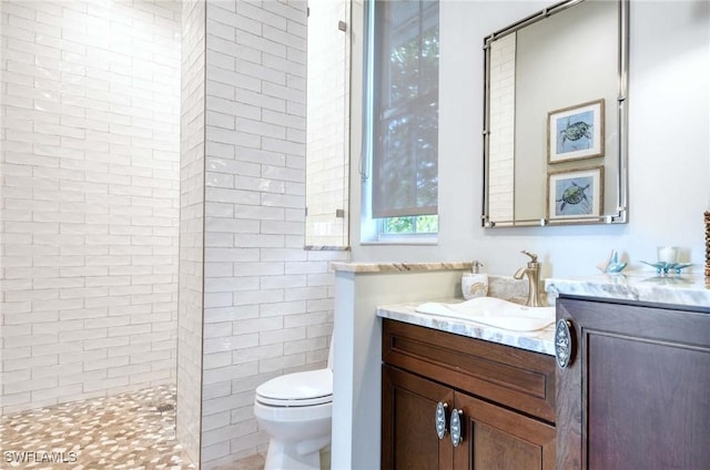 bathroom with a tile shower, vanity, and toilet