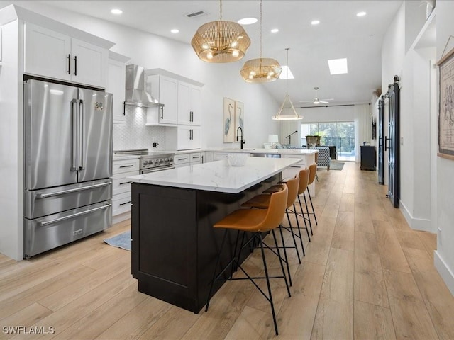 kitchen with kitchen peninsula, wall chimney exhaust hood, stainless steel appliances, decorative light fixtures, and white cabinets