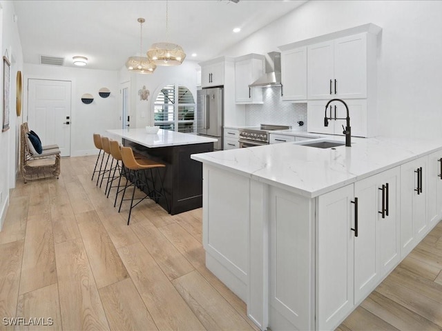 kitchen with white cabinets, wall chimney range hood, hanging light fixtures, light stone countertops, and appliances with stainless steel finishes