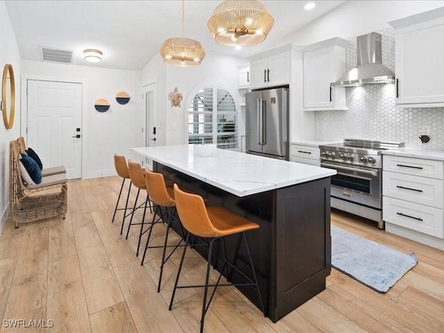 kitchen featuring wall chimney exhaust hood, high end appliances, white cabinetry, and a chandelier