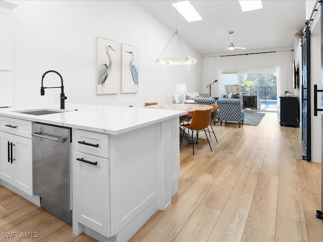 kitchen with pendant lighting, white cabinets, sink, light stone countertops, and light wood-type flooring