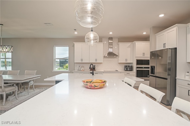 kitchen with appliances with stainless steel finishes, a wealth of natural light, hanging light fixtures, and wall chimney range hood