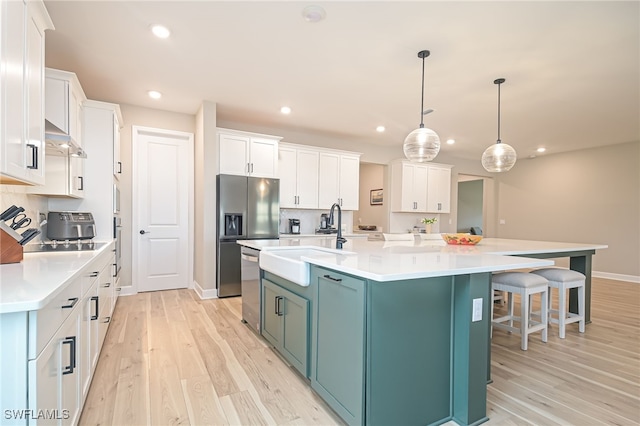 kitchen featuring a large island with sink, white cabinets, hanging light fixtures, sink, and light hardwood / wood-style flooring