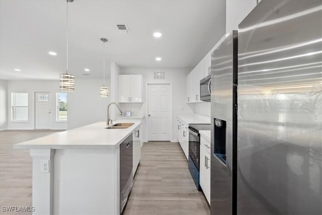 kitchen featuring stainless steel appliances, sink, white cabinets, hanging light fixtures, and an island with sink