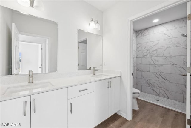 bathroom with a tile shower, ceiling fan, wood-type flooring, toilet, and vanity