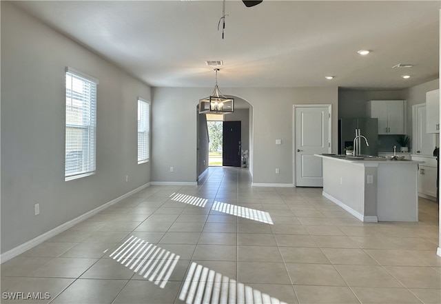 interior space featuring hanging light fixtures, white cabinets, refrigerator with ice dispenser, an island with sink, and light tile patterned flooring