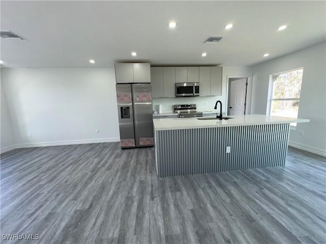 kitchen with sink, hardwood / wood-style flooring, gray cabinets, stainless steel appliances, and a center island with sink