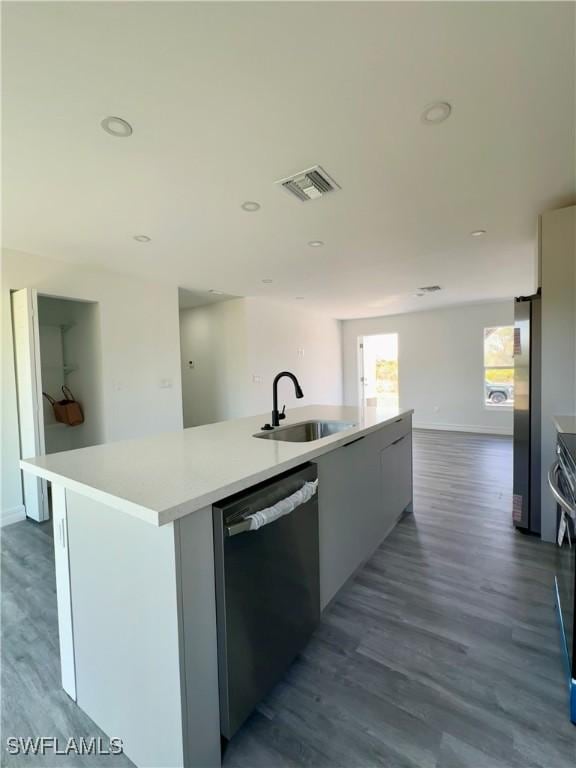 kitchen with a kitchen island with sink, sink, dishwashing machine, and stainless steel fridge