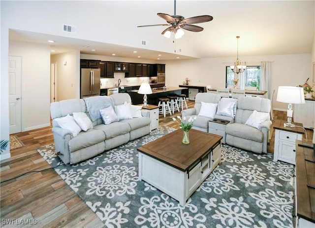 living room featuring hardwood / wood-style floors, ceiling fan with notable chandelier, high vaulted ceiling, and sink