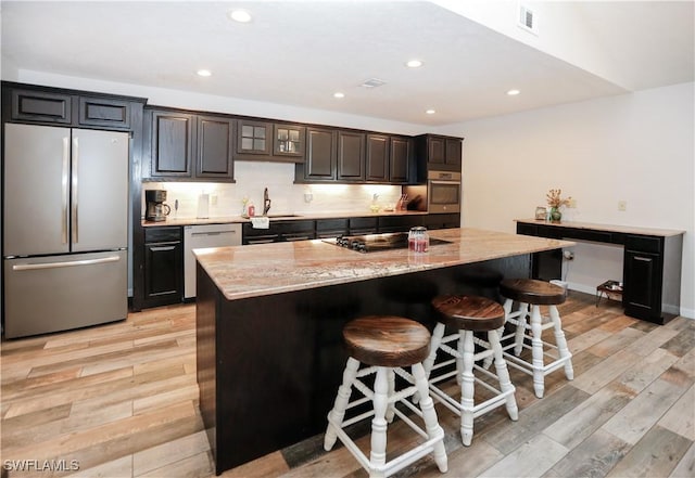 kitchen featuring light hardwood / wood-style flooring, stainless steel appliances, an island with sink, and a breakfast bar