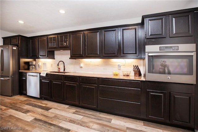 kitchen with sink, backsplash, dark brown cabinetry, stainless steel appliances, and light wood-type flooring