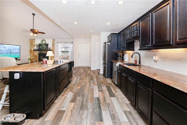 kitchen with a stone fireplace, light wood-type flooring, a kitchen breakfast bar, and appliances with stainless steel finishes