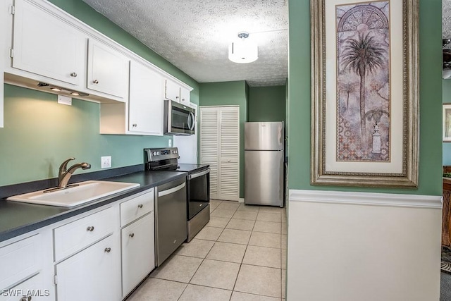 kitchen with sink, a textured ceiling, appliances with stainless steel finishes, light tile patterned flooring, and white cabinetry