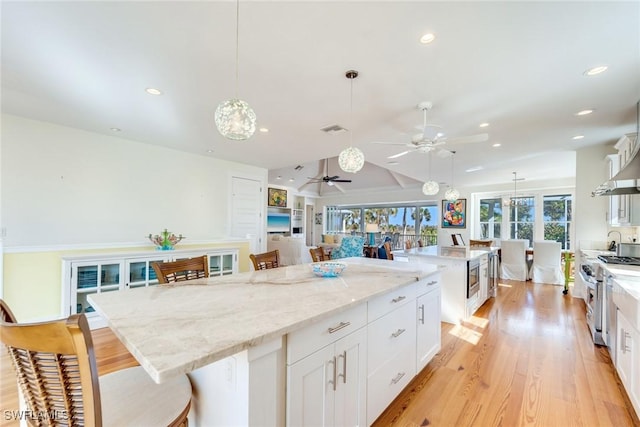 kitchen featuring a large island, hanging light fixtures, high end stainless steel range oven, white cabinets, and light wood-type flooring