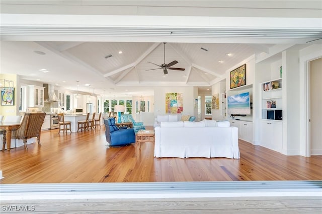 living room with lofted ceiling with beams, light hardwood / wood-style floors, built in features, and ceiling fan