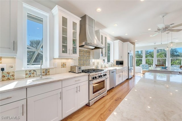 kitchen with light stone countertops, premium appliances, sink, wall chimney range hood, and white cabinetry