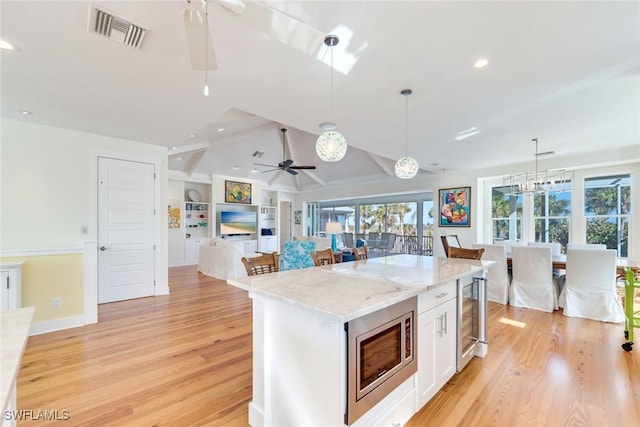 kitchen featuring stainless steel microwave, lofted ceiling with beams, light hardwood / wood-style floors, white cabinetry, and hanging light fixtures