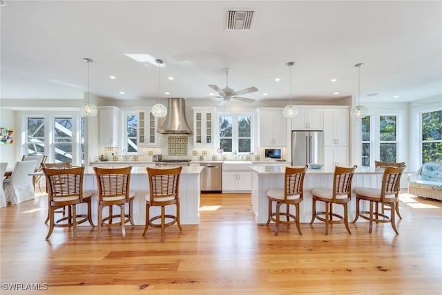 kitchen featuring decorative light fixtures, light hardwood / wood-style floors, wall chimney range hood, and stainless steel appliances