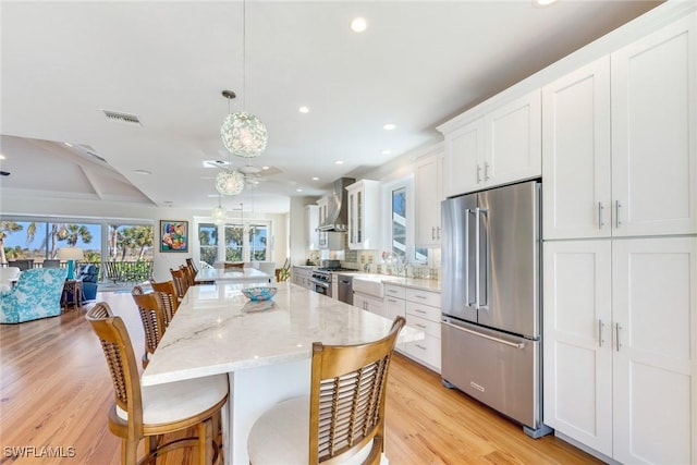 kitchen with high quality appliances, white cabinets, hanging light fixtures, light hardwood / wood-style flooring, and wall chimney exhaust hood