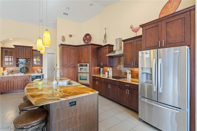 kitchen with appliances with stainless steel finishes, wall chimney range hood, tasteful backsplash, sink, and a kitchen island with sink